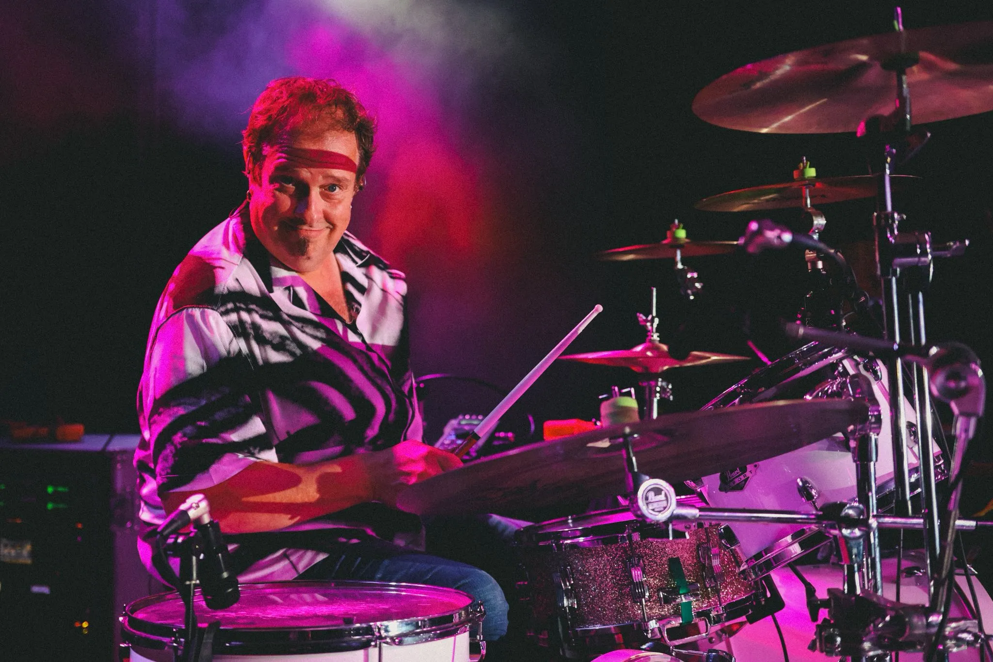 The drummer playing under magenta stage light