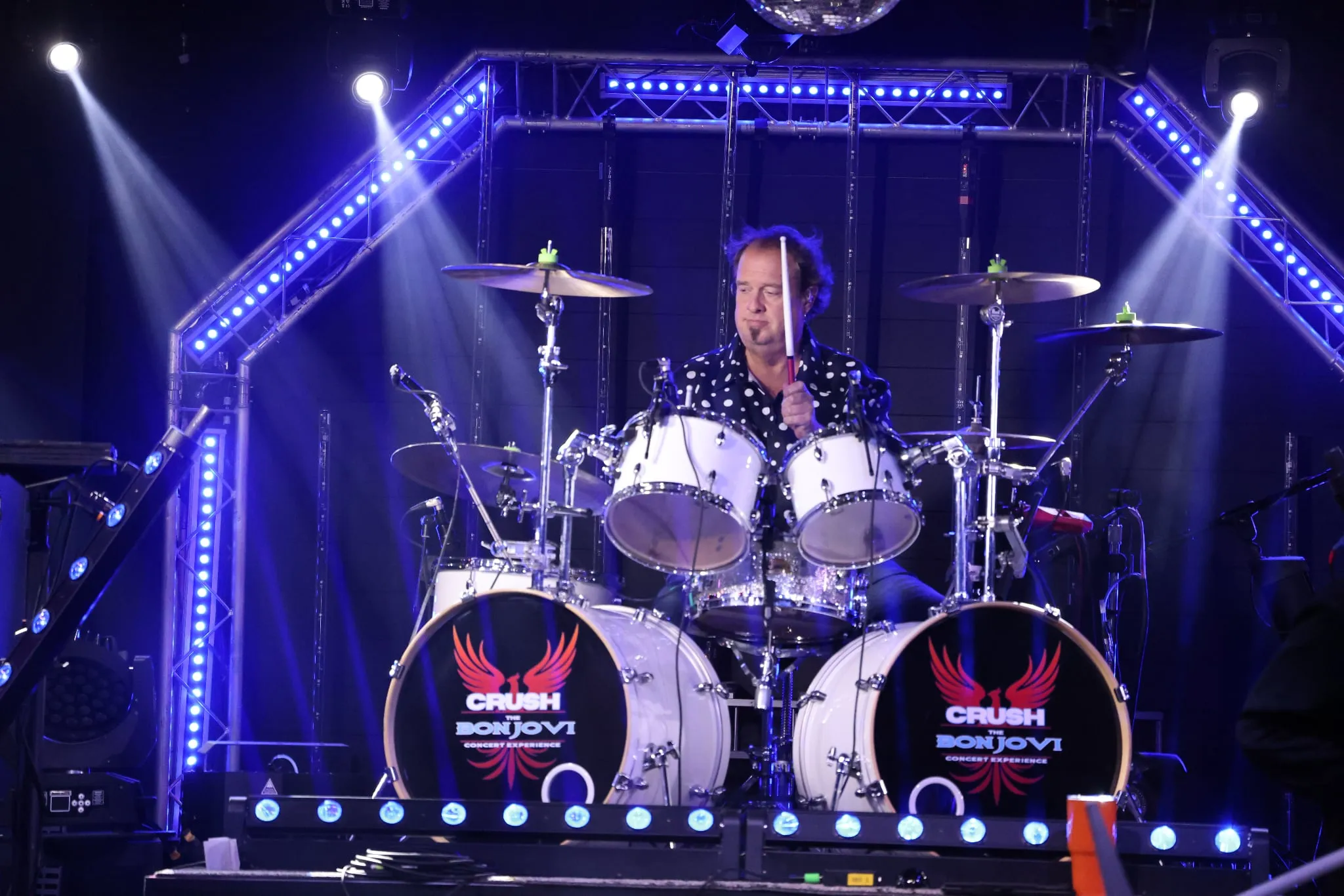 The drummer behind a kit with Crush logo drum heads, lit in blue