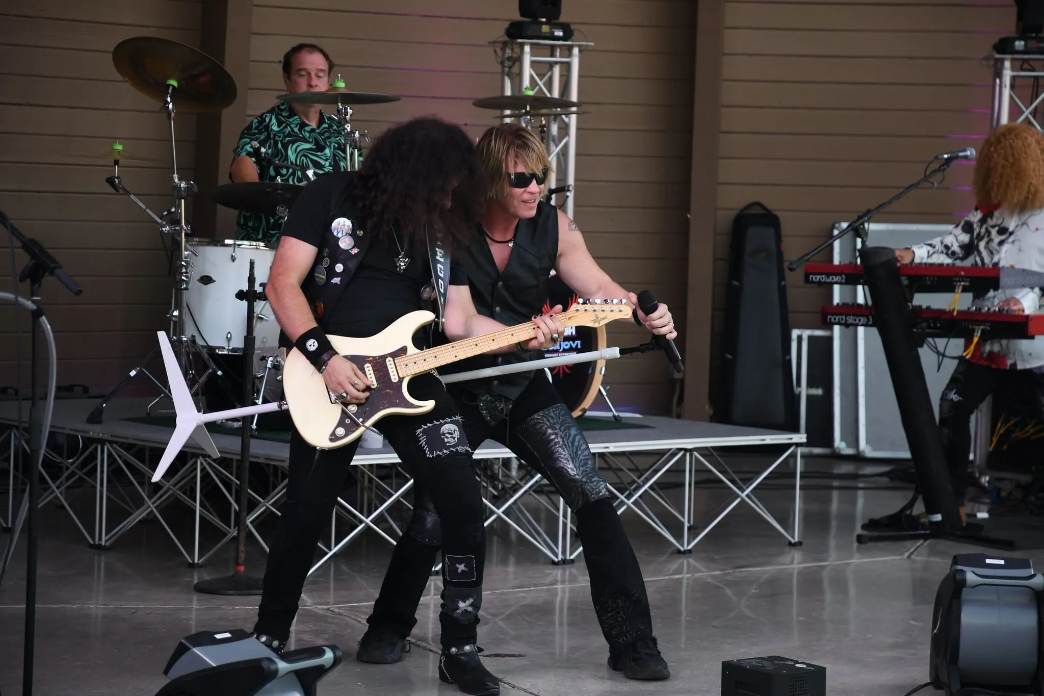 The full five-piece band performing on an outdoor stage in daylight