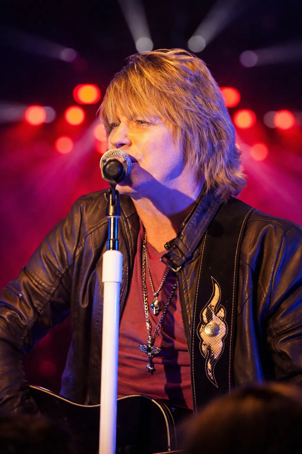 Doug Shepard singing at the mic in a leather jacket, red and purple lighting